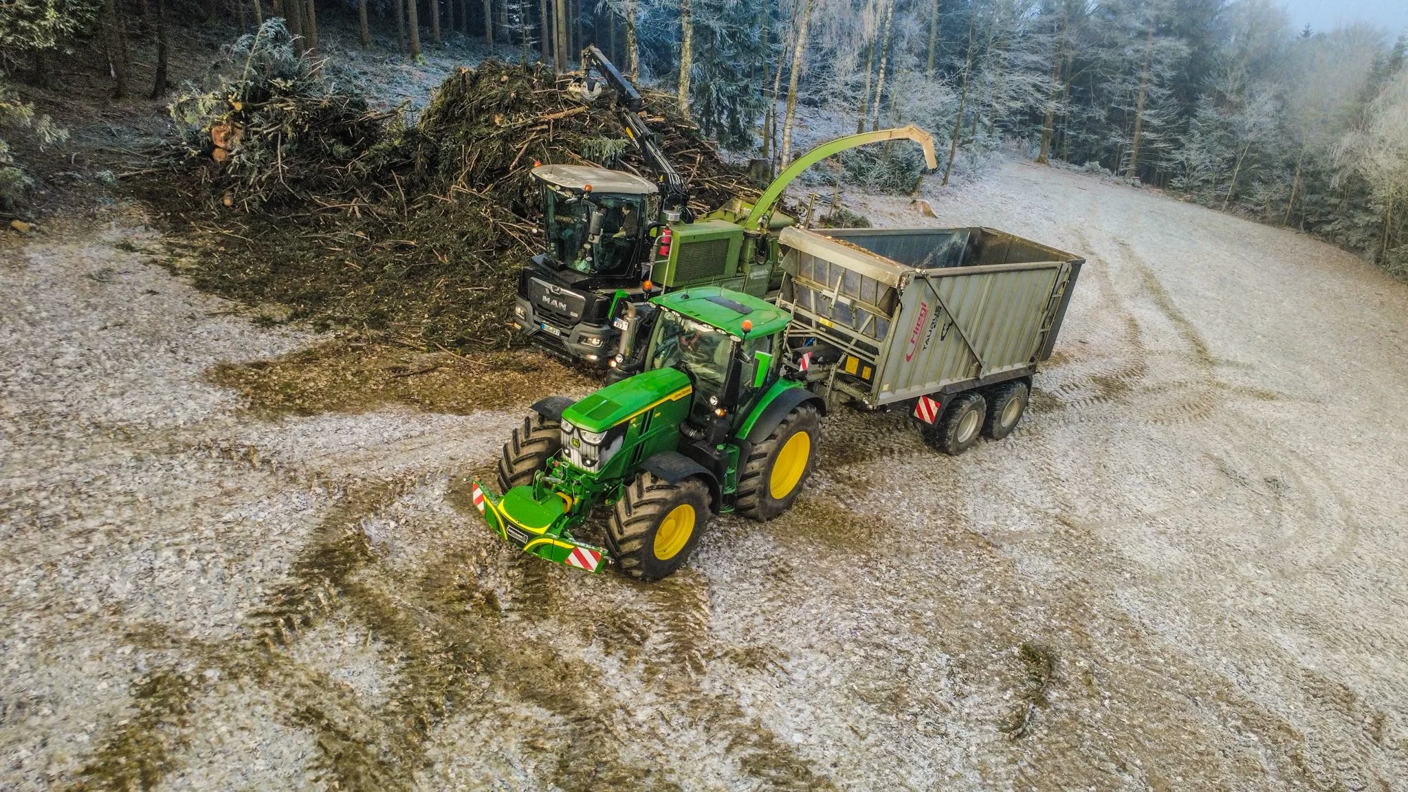Pezzolato-Holzhacker und John Deere mit Fliegl-Anhänger bei der Hackschnitzelerzeugung im winterlichen Wald